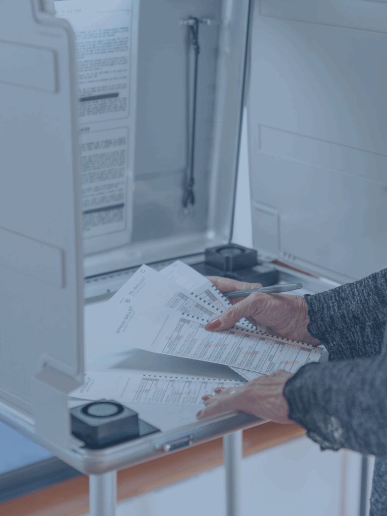 Hands of a human holding paper ballets in a voting booth.
