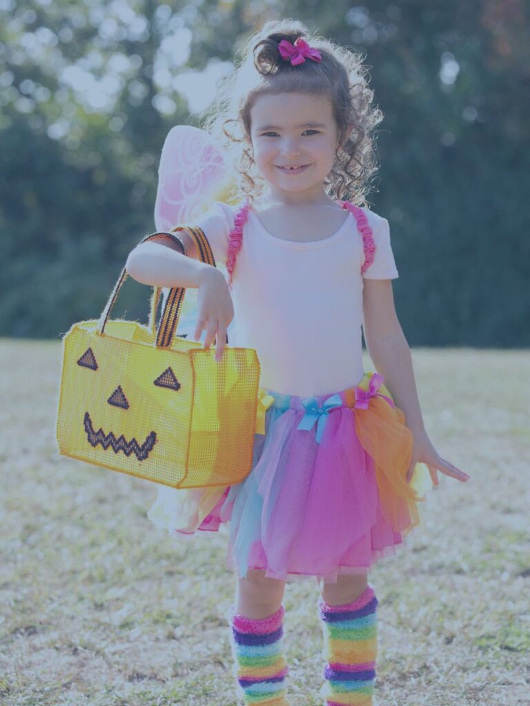 Child in colorful tutu and socks holding a pumpkin basket ready for what appears to be Halloween