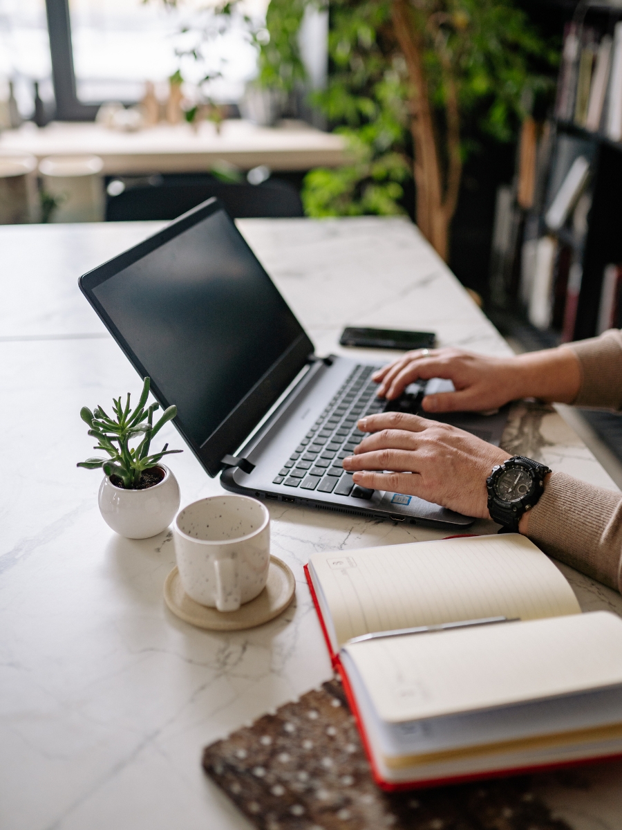 Human typing on laptop with notepad on desk