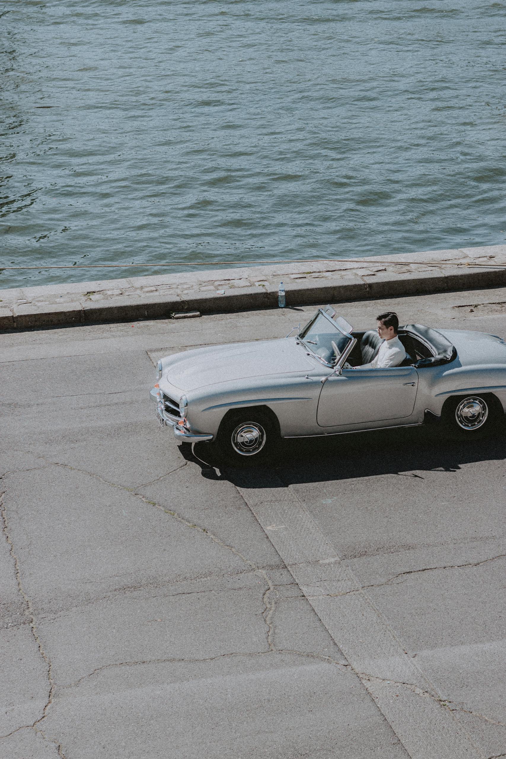 A man driving a vintage convertible on a sunny day by the riverside, enjoying freedom and adventure.