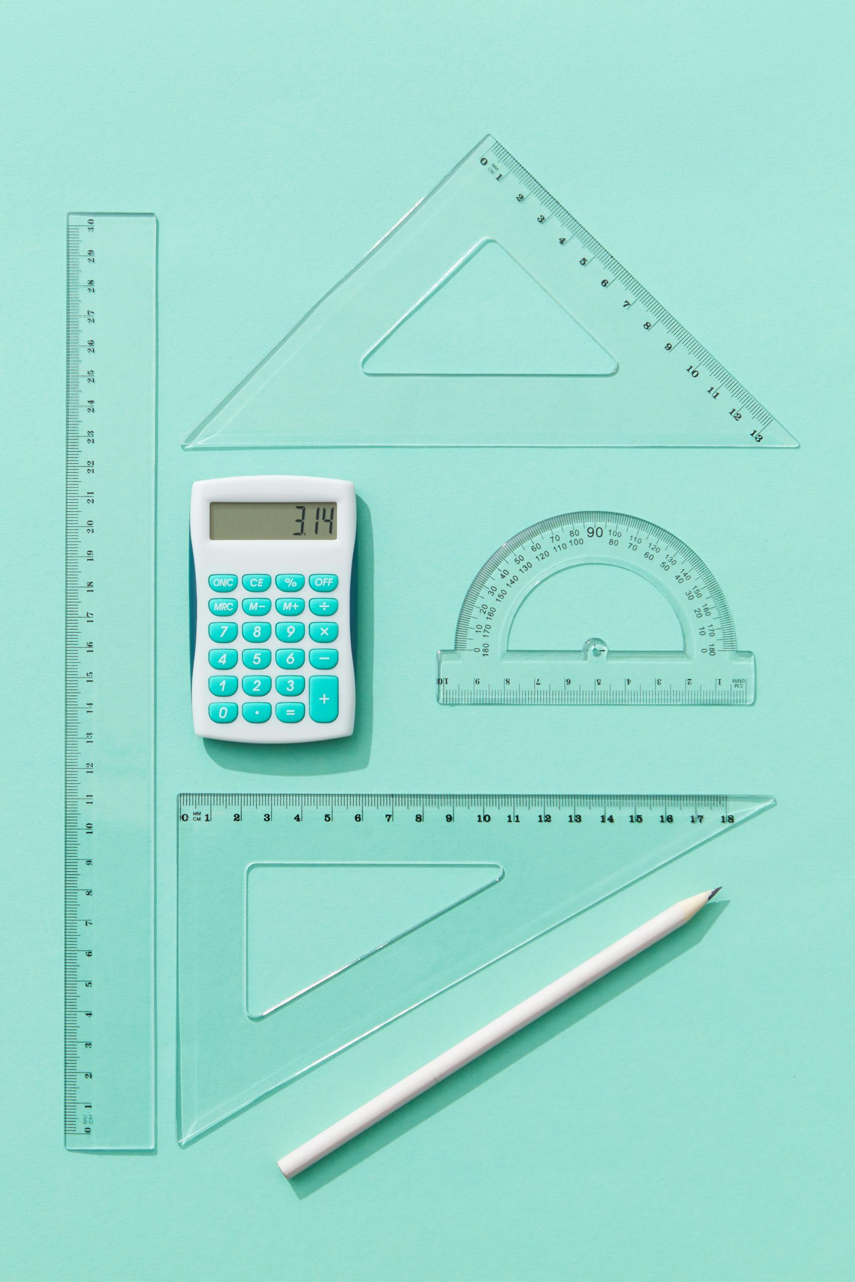 Flat lay of calculator, rulers, and protractor on teal background, ideal for educational concepts.