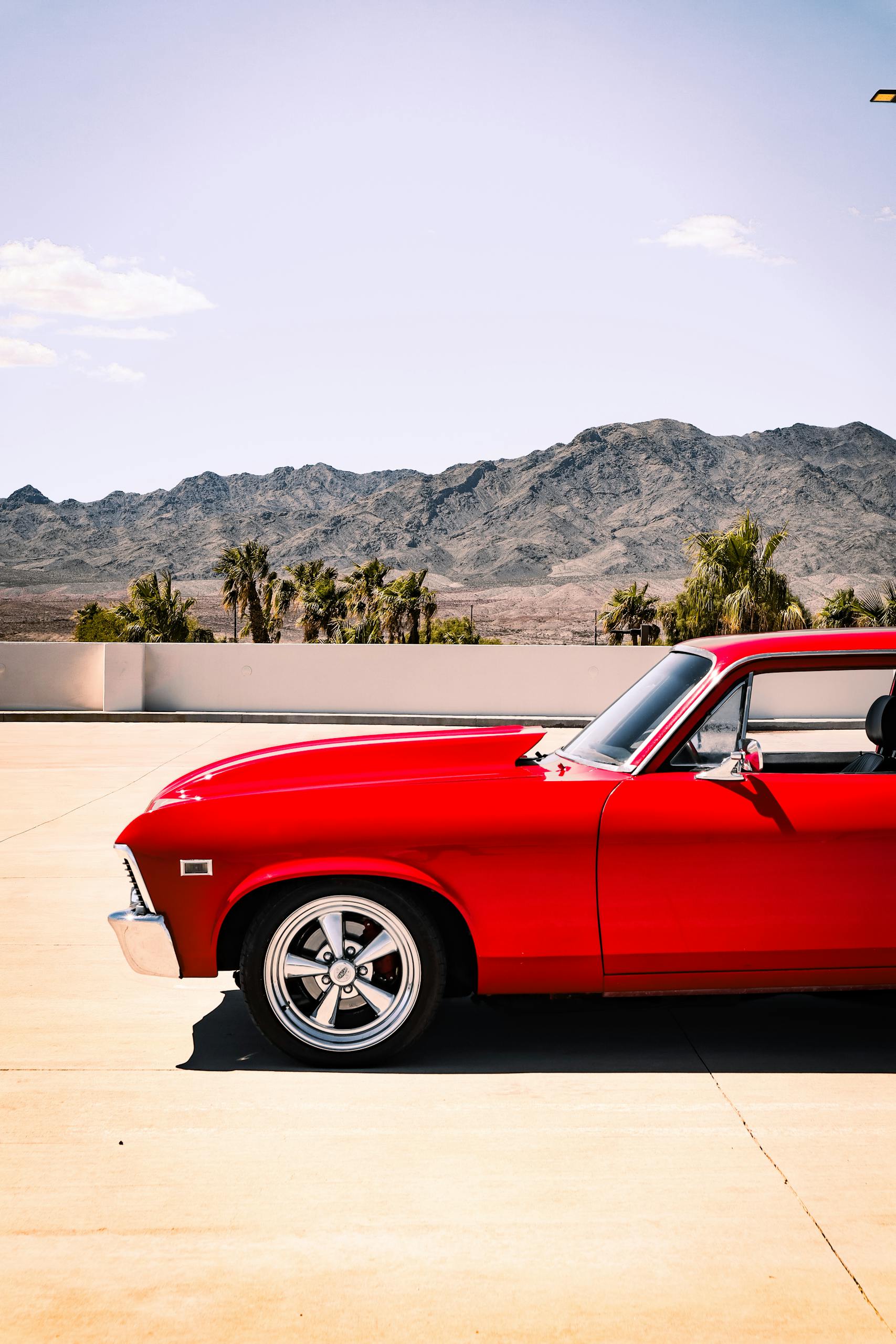 Side view of a vibrant red vintage car on a sunny desert roadside with mountains.